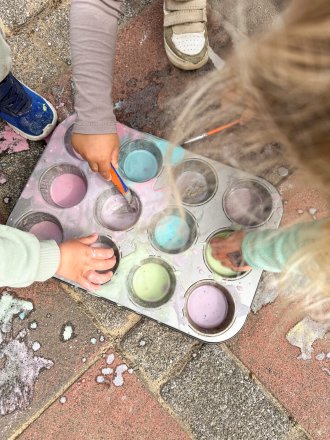 Kinder mischen bunte Farben in einer Muffinform im Freien