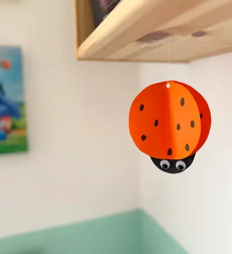 Gebastelter Marienkäfer aus Papier mit Wackelaugen hängt an einem Faden im Gruppenraum