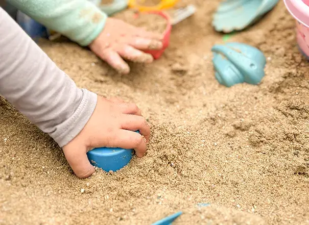 Kleines Kind spielt konzentriert im Sand – liebevolle Betreuung in natürlicher Umgebung